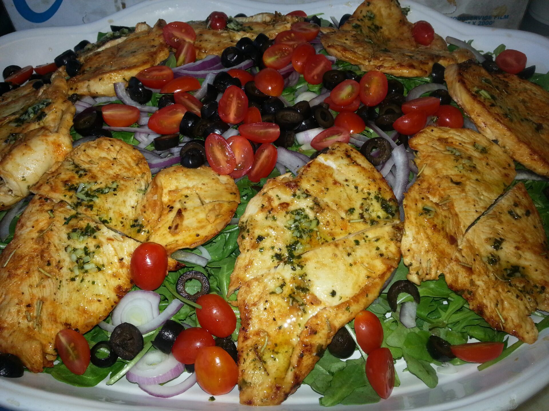 A plate of food with chicken, tomatoes and olives.