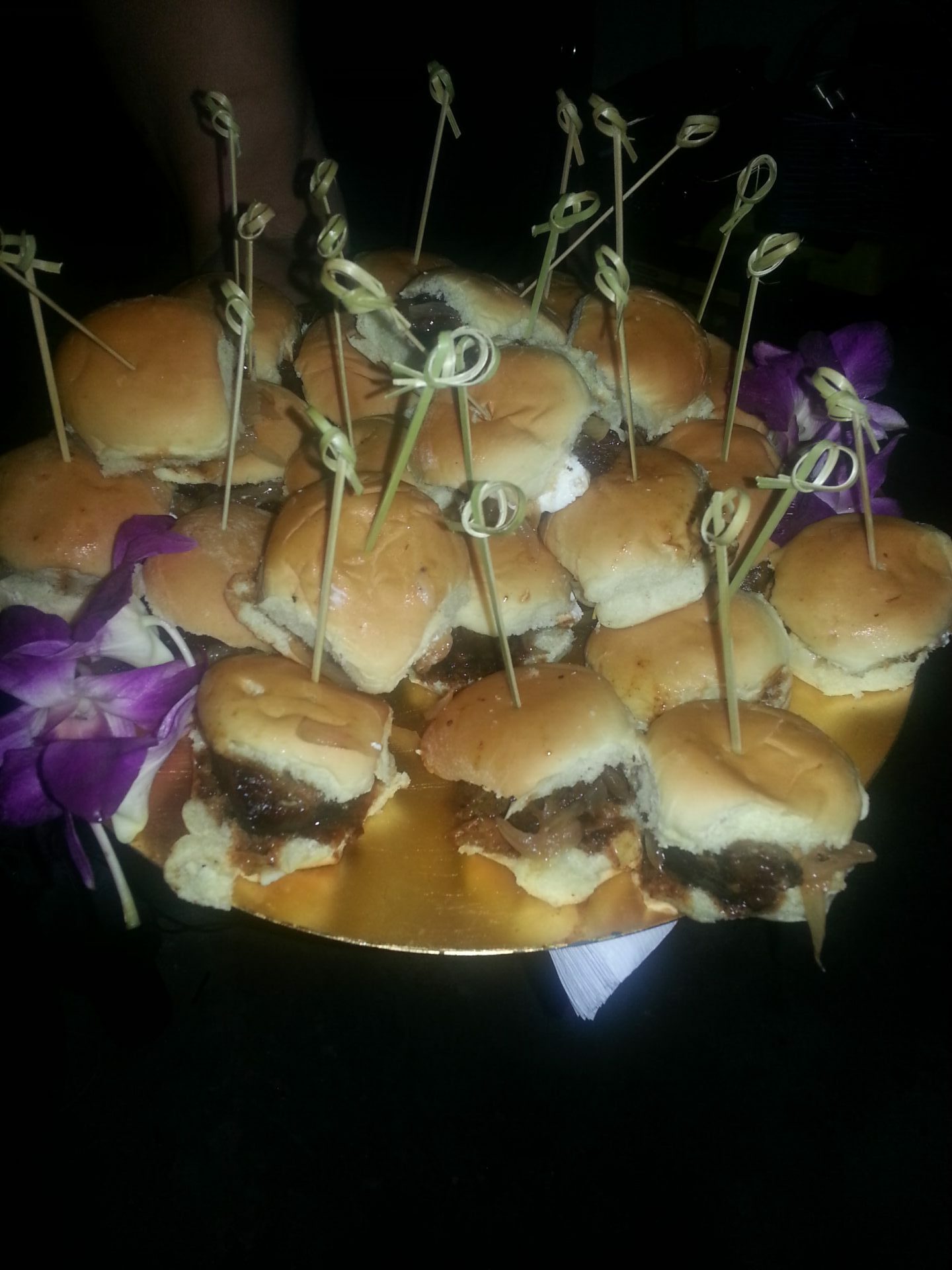 A plate full of slider burgers with picks holding each individual burger together